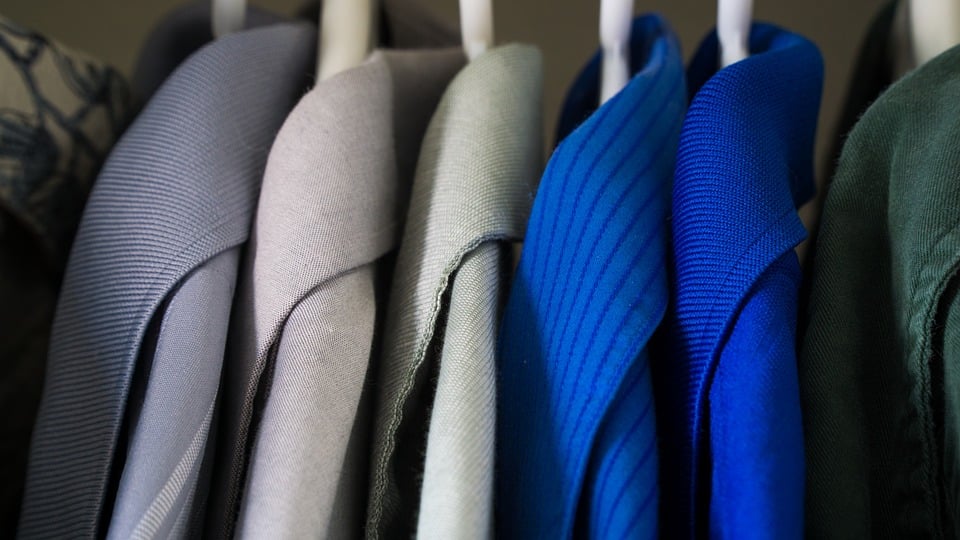 Clothing on hangers, mainly blazers, in a variety of sizes and colours