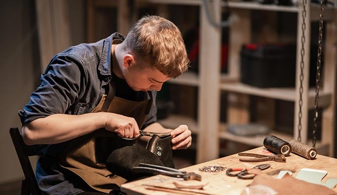 A young man is engaged in the family craft of making leather shoes in a workshop.