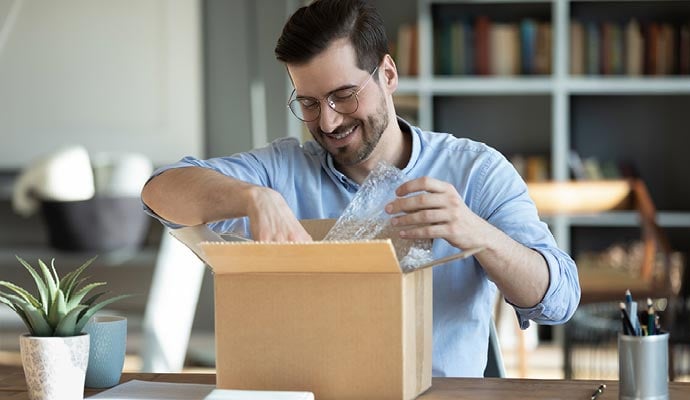 Man sat at his desk opens parcel containing an order he has bought online