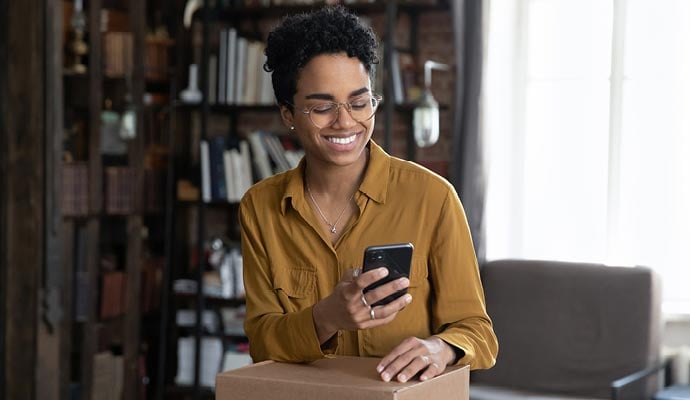 Woman sending parcel checks her phone to find the cheapest courier price