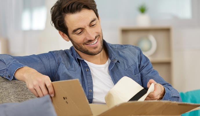 Man opening parcel containing hat which he bought online